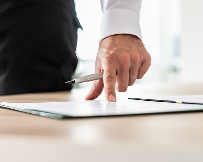 Mano sujetando bolígrafo mirando un documento a firmar sobre la mesa